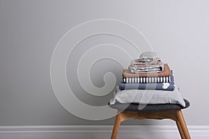 Stack of clean bed linen and pillow on stool near light grey wall. Space for text