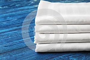 Stack of clean bed sheets on color wooden background, closeup