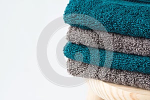 Stack of clean folded navy turquoise beige terry towels on wooden chair white wall background. Laundry spa wellness cleanliness