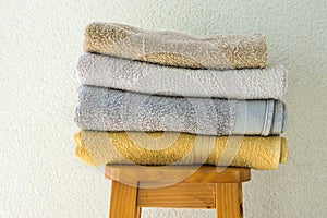 Stack of clean folded terry towels on wooden high stool white wall background. Laundry spa wellness cleanliness concept