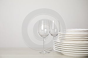 Stack of clean plates and glasses on table against background. Space for text