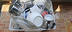 Stack of Clean Tableware on Drying Rack: Spoons, Glasses, Plates, and Bowls.
