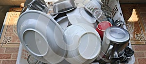 Stack of Clean Tableware on Drying Rack: Spoons, Glasses, Plates, and Bowls.