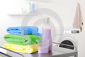 Stack of clean towels and detergent on table in laundry room.