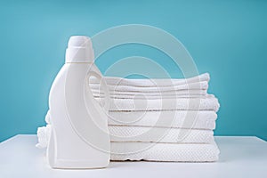 Stack of clean white towels and a bottle of detergent on blue background