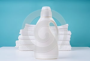 Stack of clean white towels and a bottle of detergent on blue background