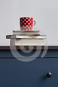 stack of closed books with tea cup on top on blue chest of drawers