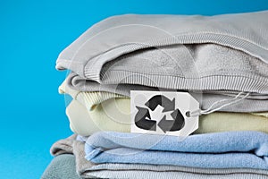 Stack of clothes with recycling label on light blue background, closeup
