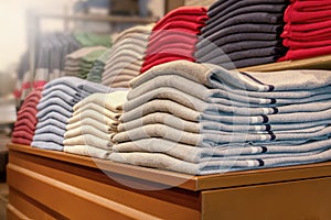 A stack of clothes in the store, pullovers and sweatshirts nicely and neatly stacked in bundles on the table and red
