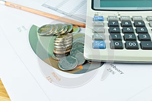 The stack of coin with business paper graphs and pencil with charts report, calculator, concept of calculating expenses