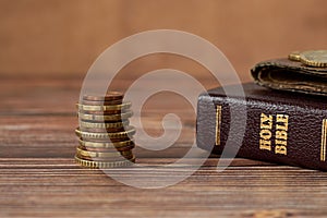 Stack of coin money, holy bible book and old wallet on wooden table, a closeup