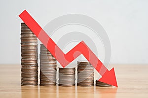 Stack of coins bar chart and red graph trending downwards with white wall background on wooden table copy space. Economy recession