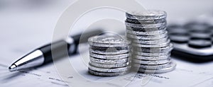 The stack of coins beside a calculator and pen on financial documents. AI generated image