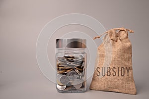 Stack of coins in a glass jar and money bag with text SUBSIDY