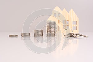 Stack of coins and a key on a gray background with model house with reflection