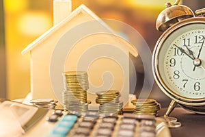 Stack of coins planing to buy home with clock and house model