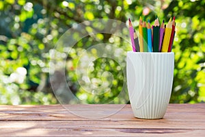 Stack of colored pencils in a glass on green natural background.