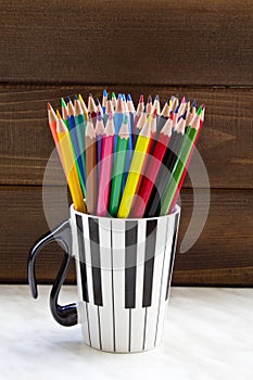 Stack of colored pencils in a glass on wooden background.