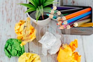 Stack of colored pens marker In a metal case, crumple paper and artificial plant on wooden desk