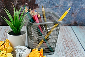 Stack of colored pens marker In a metal case, crumple paper and artificial plant on wooden desk