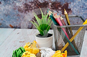 Stack of colored pens marker In a metal case, crumple paper and artificial plant on wooden desk