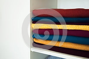 A stack of colored things, clothes, neatly stacked on a shelf in a white wardrobe.