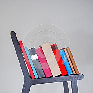 Stack of colorful books on black wooden chair.