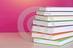 Stack of colorful books, bright colorful pink background, free copy space. Books on table, no labels, blank spine. Back to school
