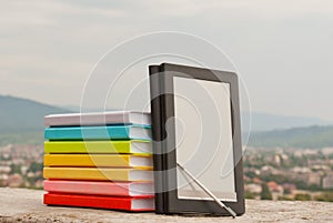 Stack of colorful books with e-book reade