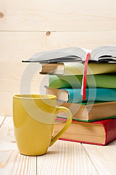 Stack of colorful books, open book and cup on wooden table