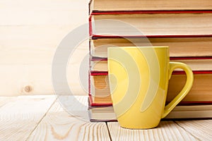 Stack of colorful books, open book and cup on wooden table