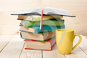 Stack of colorful books, open book and cup on wooden table. Back to school. Copy space