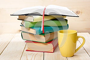 Stack of colorful books, open book and cup on wooden table. Back to school. Copy space