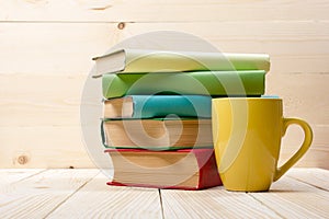 Stack of colorful books, open book and cup on wooden table. Back to school. Copy space