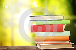 Stack of colorful books on wooden table against green background. Space for text