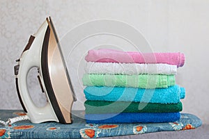 Stack of colorful clean towels on grey background. Ironing clothes on ironing board. Stack of clean towels on table.