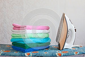 Stack of colorful clean towels on grey background. Ironing clothes on ironing board. Stack of clean towels on table.