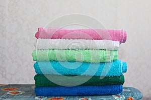 Stack of colorful clean towels on grey background. Ironing clothes on ironing board. Stack of clean towels on table.