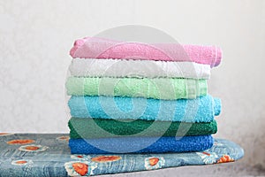 Stack of colorful clean towels  on grey background. Ironing clothes on ironing board. Stack of clean towels on table.