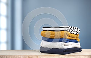 Stack of colorful knitted folded clothes on wooden table empty space blue background. Winter apparel