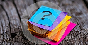 Stack of colorful sticky notes on wooden background with a prominent blue note featuring a black question mark symbolizing