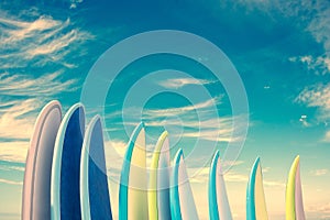 Stack of colorful surfboards on blue sky background with copy space, retro vintage filter