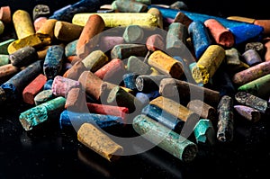 Stack of colorful used pastel crayons on a reflective black background