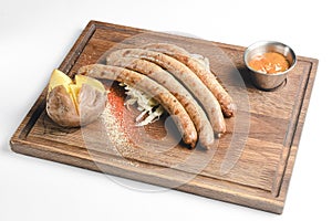 Stack of cooked sausages served on a rustic wooden board with sauce and baked potatoes.