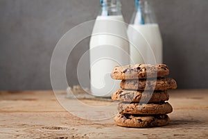 A stack of cookies with milk chocolate and two bottles of milk on a wooden table