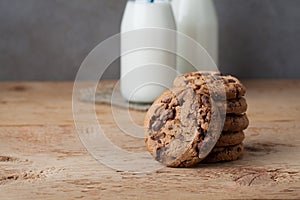 A stack of cookies with milk chocolate and two bottles of milk on a wooden table