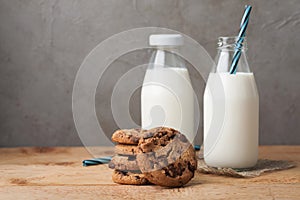 A stack of cookies with milk chocolate and two bottles of milk on a wooden table with copy space
