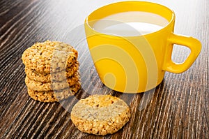 Stack of cookies with sesame and flax seeds, cup with milk on wooden table