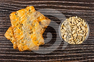 Stack of cookies with sunflower seeds and bowl with peeled seeds on dark wooden table. Top view