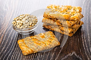 Stack of cookies with sunflower seeds, bowl with peeled seeds on wooden table